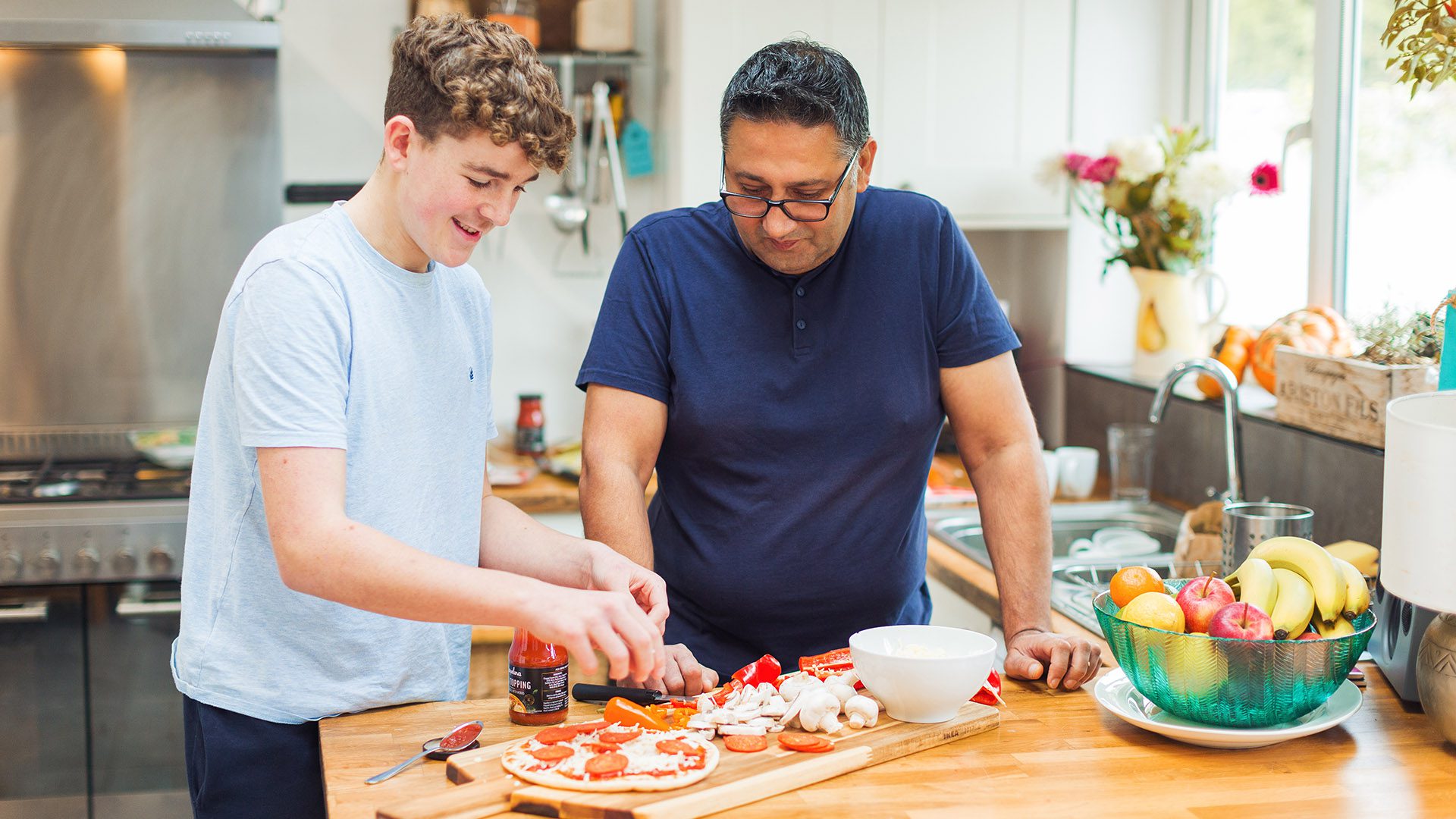 Man and teenager making pizza in a kitchen